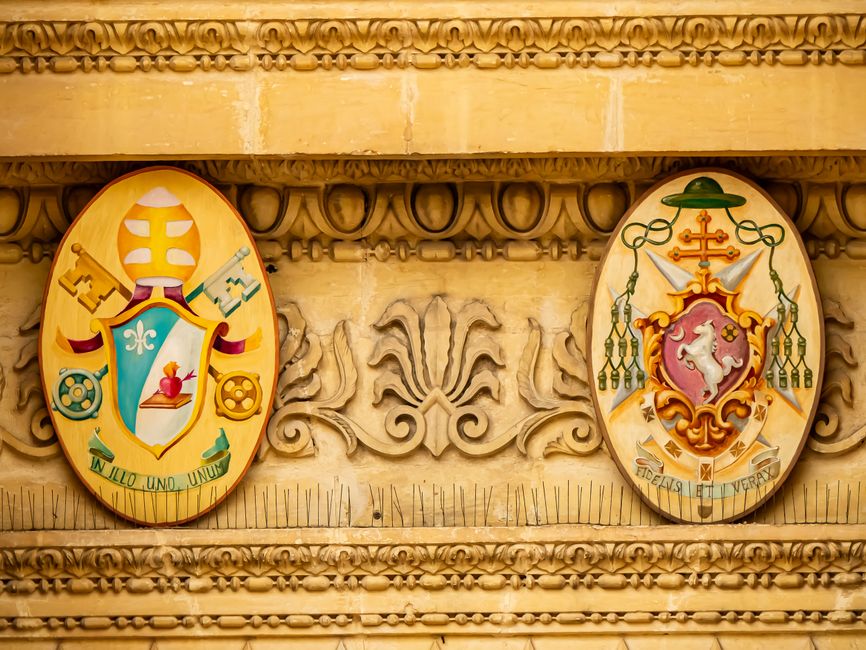 Ornate architectural carvings displaying vibrant heraldic symbols on a historic wall.