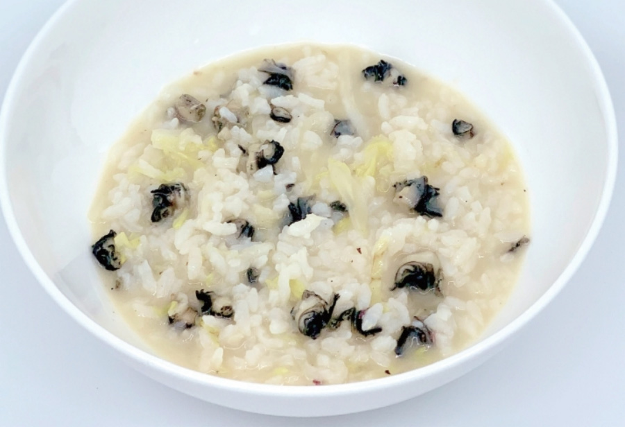 야생에서 채취를 한 우렁이를 잘 손질을 한 후에 쌀과 함께 넣고 끓여서 만든 우렁이죽을 하얀 그릇에 반쯤 담아둔 것을 흰색 바닥 위에 놓아두고 찍은 사진