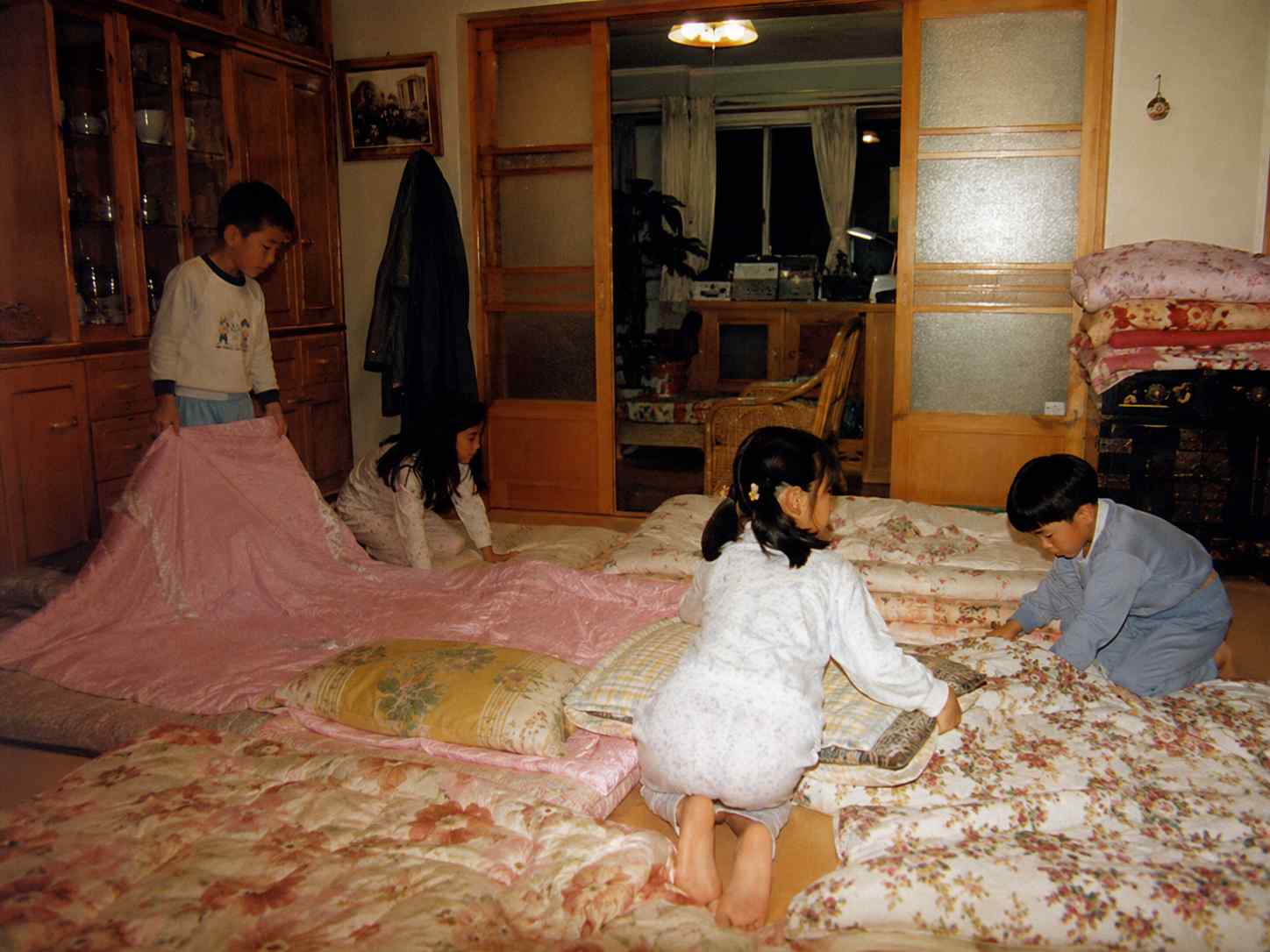 친척집 방바닥에 여러 채의 이불을 펴며 잠자리를 준비하는 아이들