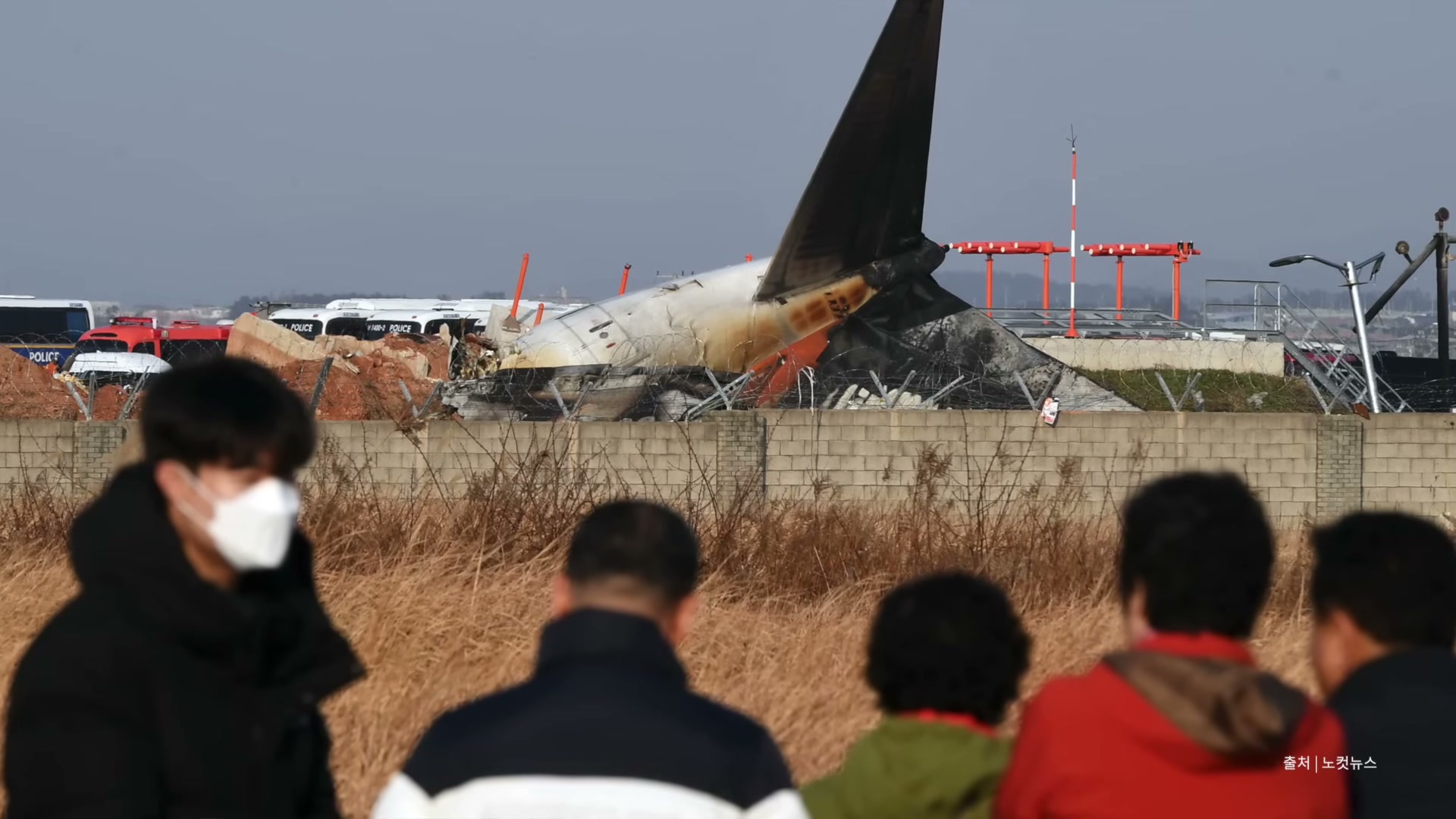 마스크를 쓴 시민들이 사고 여객기 잔해를 멀리서 바라보는 뒷모습