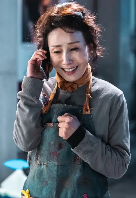 갈색 웨이브 머리를 묶고 회색 상에와 피묻은 작업복을 입고 전화를 받고 있는 드라마 7인의 탈출의 정미소 캐릭터