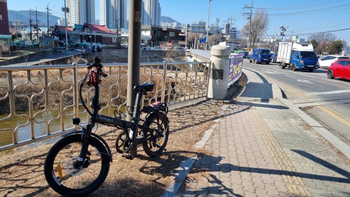 가금교 난간 앞 가로등 기둥에 타고온 자전거 매어놓았음, 오후의 햇살에 길게 누운 그림자, 우측에 가금교에서 넘어오는 승용차들,