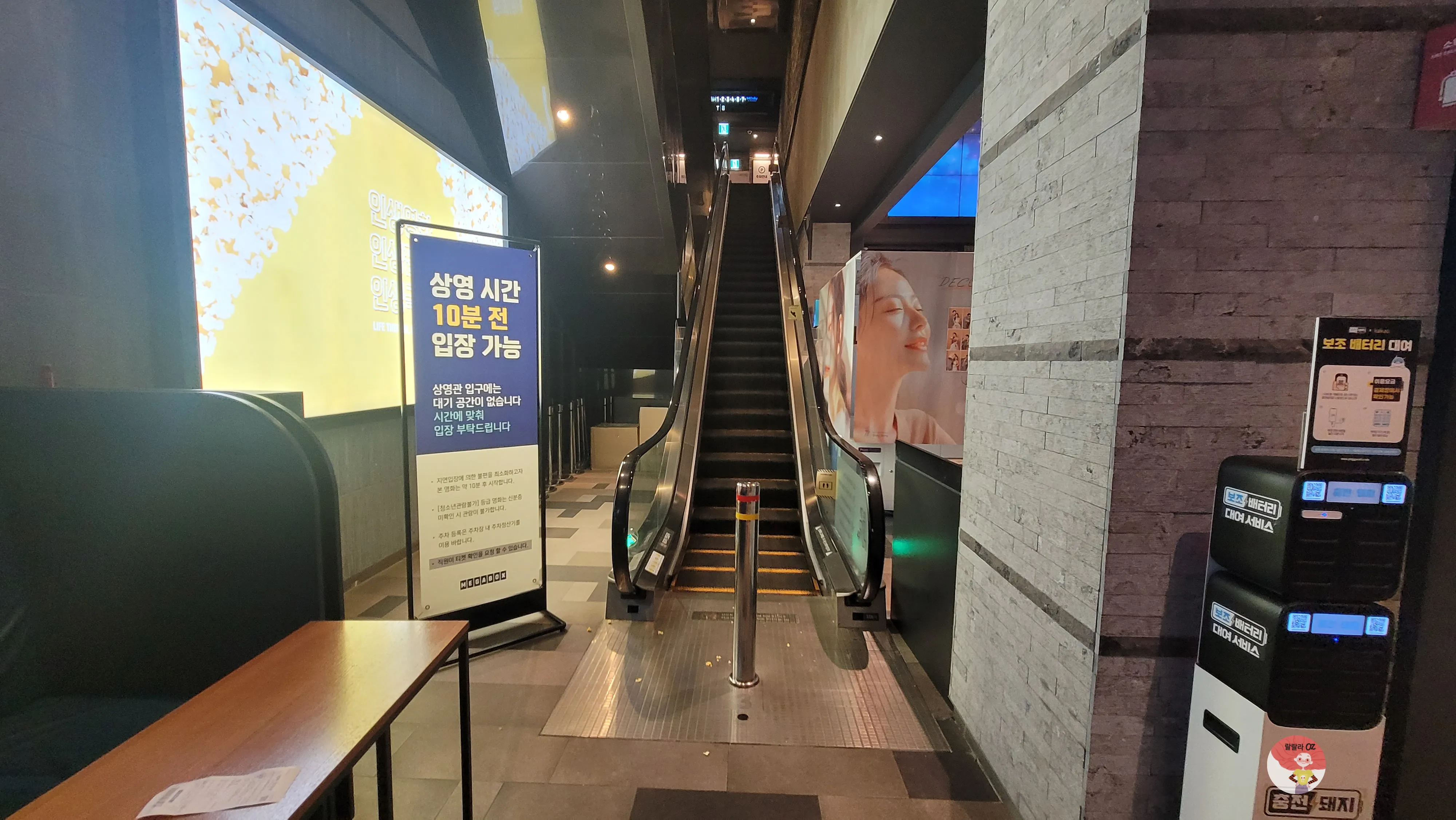 다산아울렛 메가박스 내부, 상영관으로 올라가는 에스컬레이터와 입장 안내 표지판이 보이는 모습