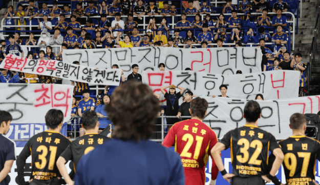 자신을 비판하는 걸개가 걸린 응원석을 바라보고 있는 홍명보