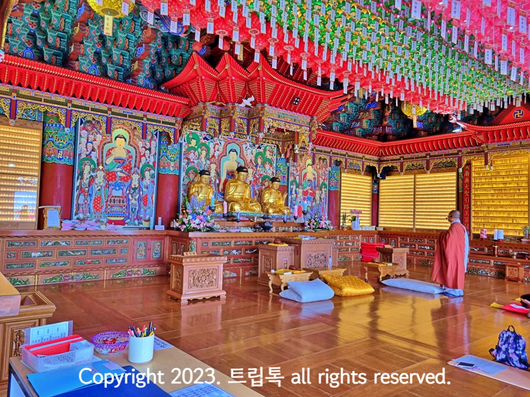 천장에 빼곡히 등이 달려있고 가운데 세개의 불상이 있다. 오른쪽에 스님이 서있다.