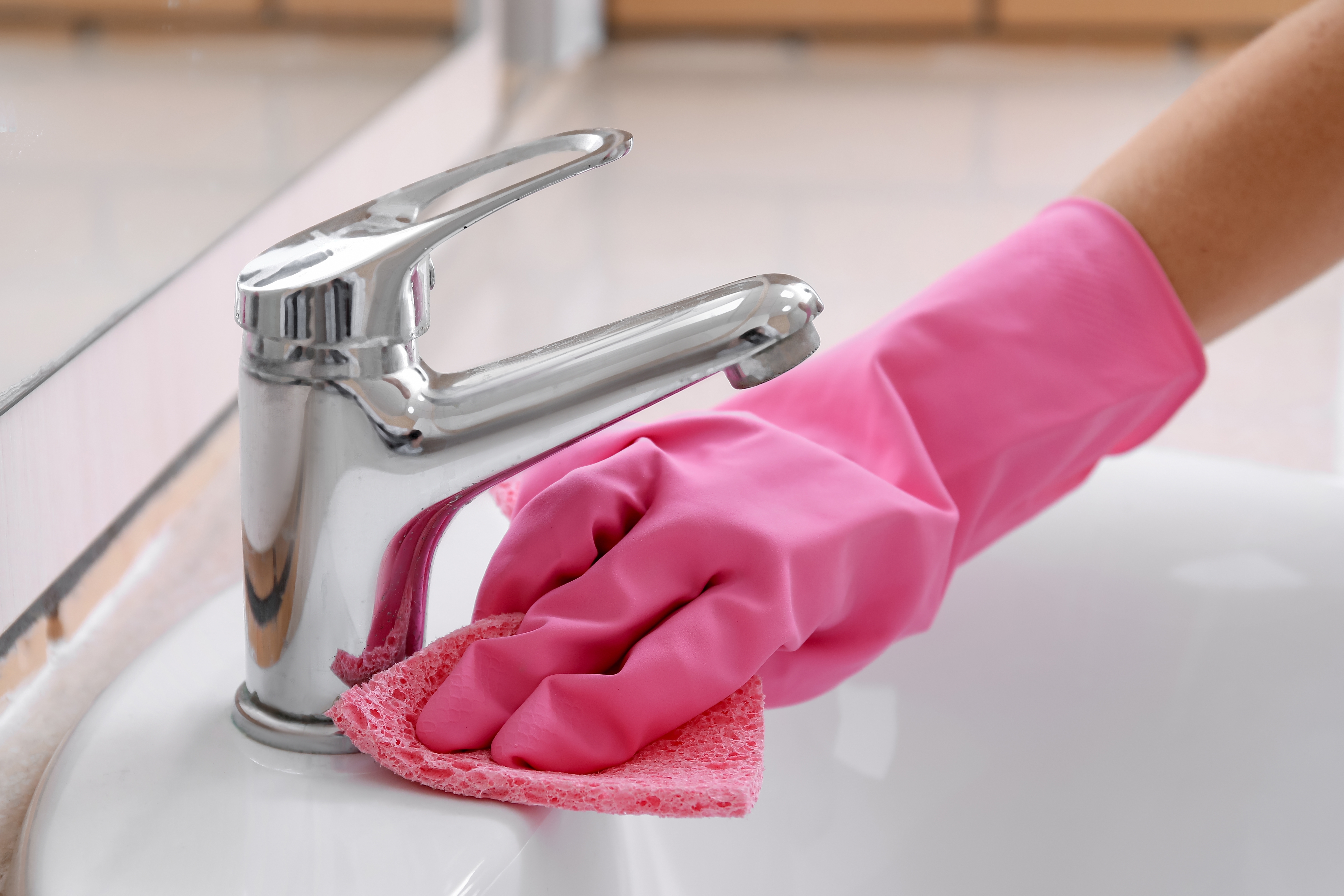 분홍 고무장갑을 낀 손이 욕실 세면대 수전을 스펀지로 청소하는 모습, 곰팡이 제거 청소 루틴