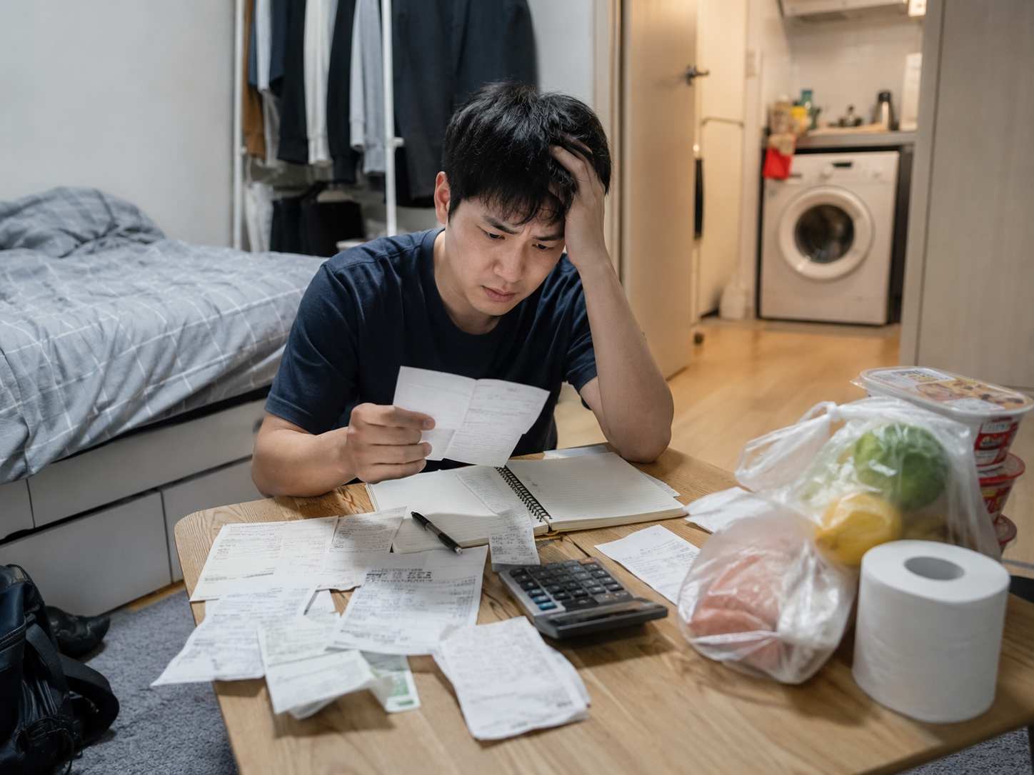 자취방 테이블에 영수증과 계산기를 펼쳐 놓고 생활비를 계산하는 청년