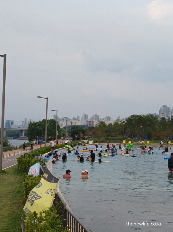 한강과 연결된 잠실 한강공원 물놀이장 옆 강변 풍경 &ndash; 시민들이 가까운 거리에서 물놀이 중인 장면