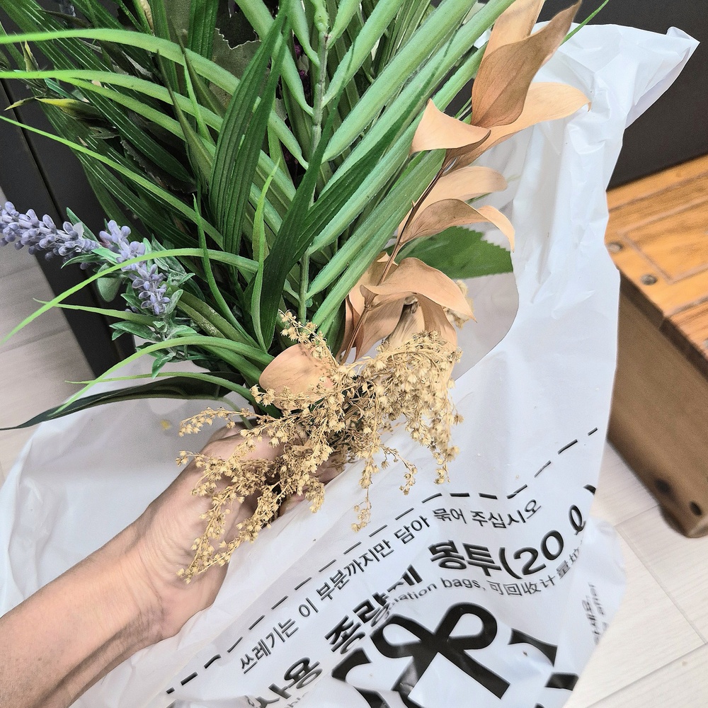 시든 생화와 인테리어 조화를 종량제 봉투에 담아 일반쓰레기로 정리하는 모습