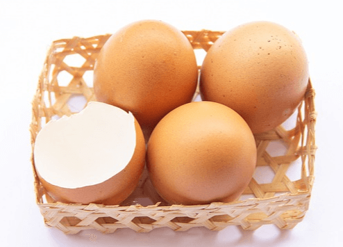 작은 갈색 바구니에 갈색 달걀 3개와 달걀 껍데기 1개가 놓여있다.