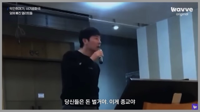 다큐 《악인취재기: 사기공화국》에서 연단 위 연설자가 "당신들은 돈 벌 거야. 이게 종교야"라고 외치는 장면. 돈이 신앙이 되고, 욕망이 교리가 된 사회의 민낯을 적나라하게 드러낸다.