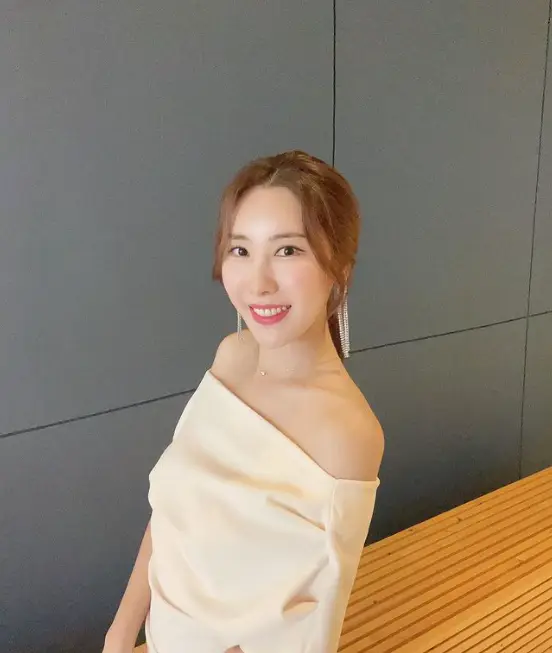 현역가왕- 회색 복도 어깨가 드러난 아이보리원피스를 입고 카메라를 향해 미소짓는 주미