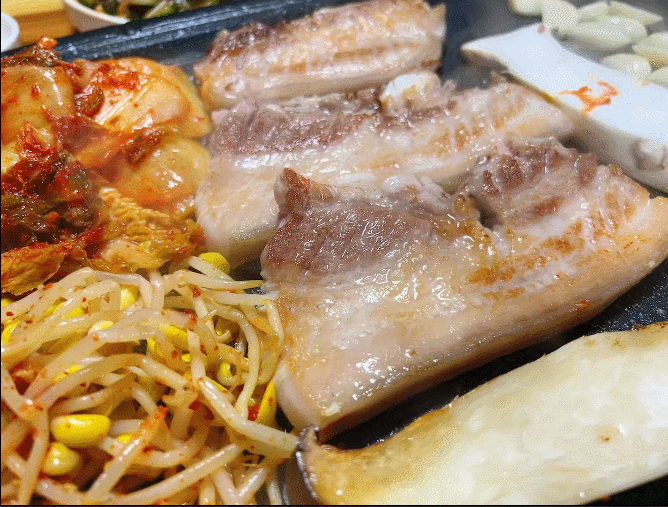 불판에서 맛있게 구워지는 삼겹살과 김치&amp;#44; 콩나물무침&amp;#44;새송이버섯&amp;#44; 마늘