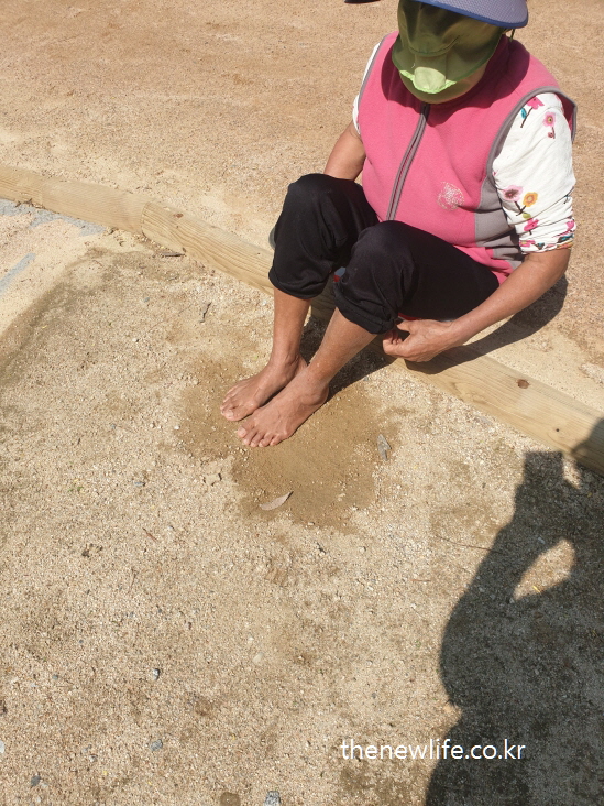 Elderly woman relaxing barefoot after earthing at Amsa Prehistoric Site-암사 선사 유적지에서 맨발 걷기 후 흙 위에 앉아 휴식하는 어르신의 모습