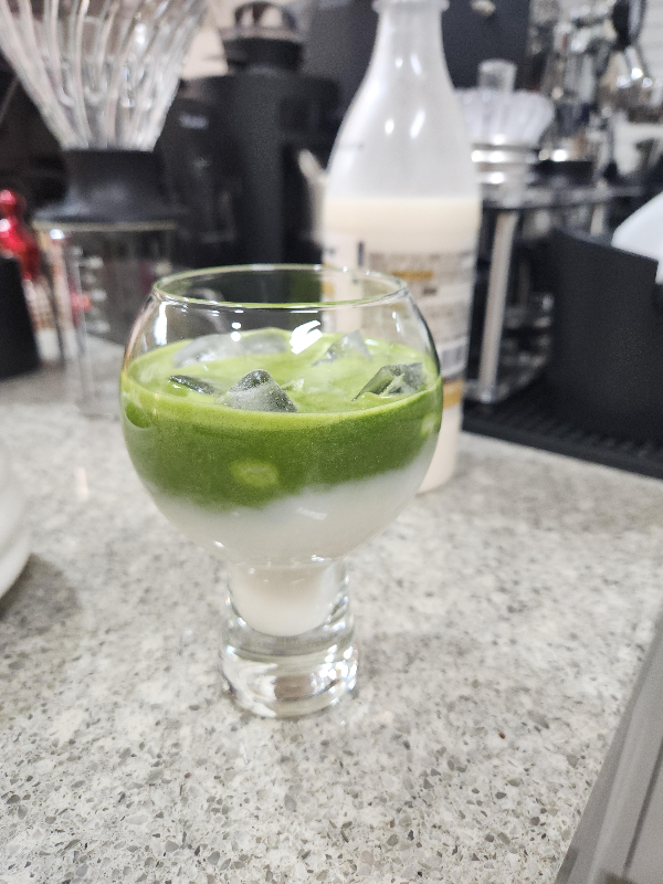 테이블 위에 막걸리와 말차가 담긴 유리컵 그리고 느린마을 막걸리가 놓여 있다.