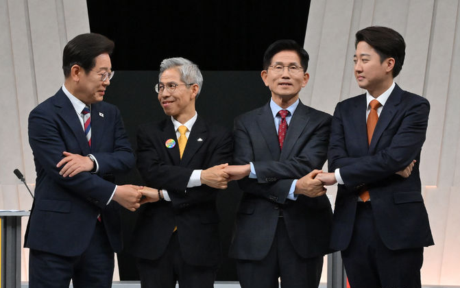 2025년 대선 후보 토론회에서 정장 차림의 네 명의 후보자들이 무대 위에서 서로 손을 맞잡고 서 있는 모습. 각기 다른 색상의 넥타이를 착용한 후보자들이 토론 전 포즈를 취하고 있다