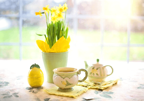 탁자에 노란 수선화가 가득한 하얀 도지가병이 있고 왼쪽엔 메밀차가 담긴 찻잔이 있다.
