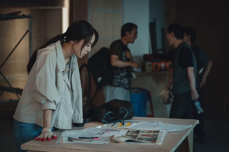 인테리어 현장의 작업자들을 배경으로 책상에 서서 도면을 바라보고 있는 영화 타겟의 장수현