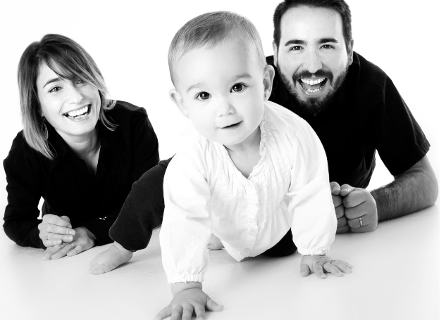 밝게 웃고 있는 부모와 기어가는 아기의 흑백 가족 사진