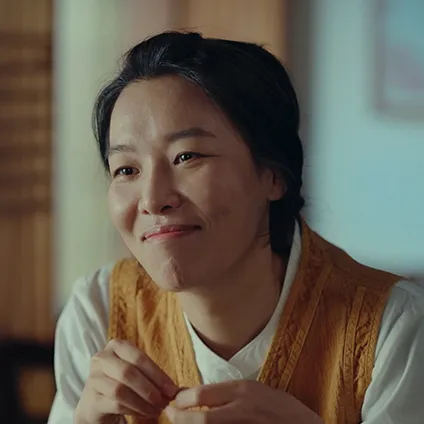 어느 집 실내를 배경으로 노란 조끼 가디건을 걸치고 발게 미소 짖고 있는 김애경