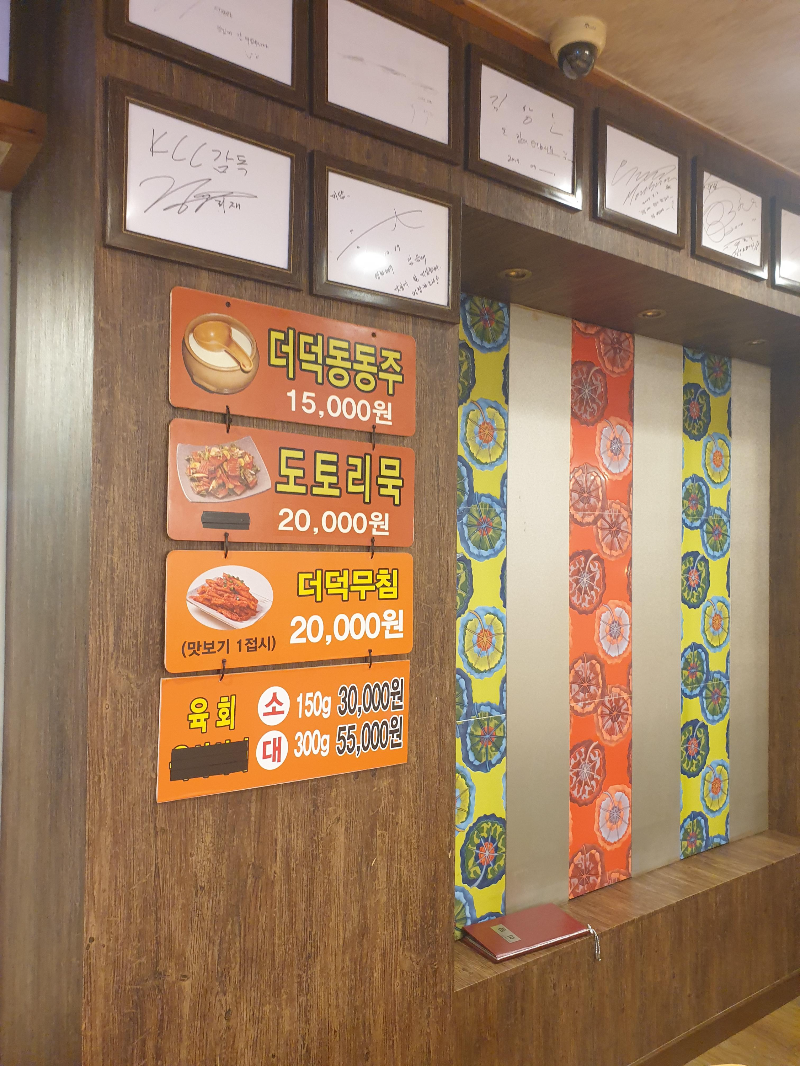 유명인 사인과 서브 메뉴명이 벽에 붙어 있다. 더덕동동주, 도토리묵, 더덕무침 등이 써있다.