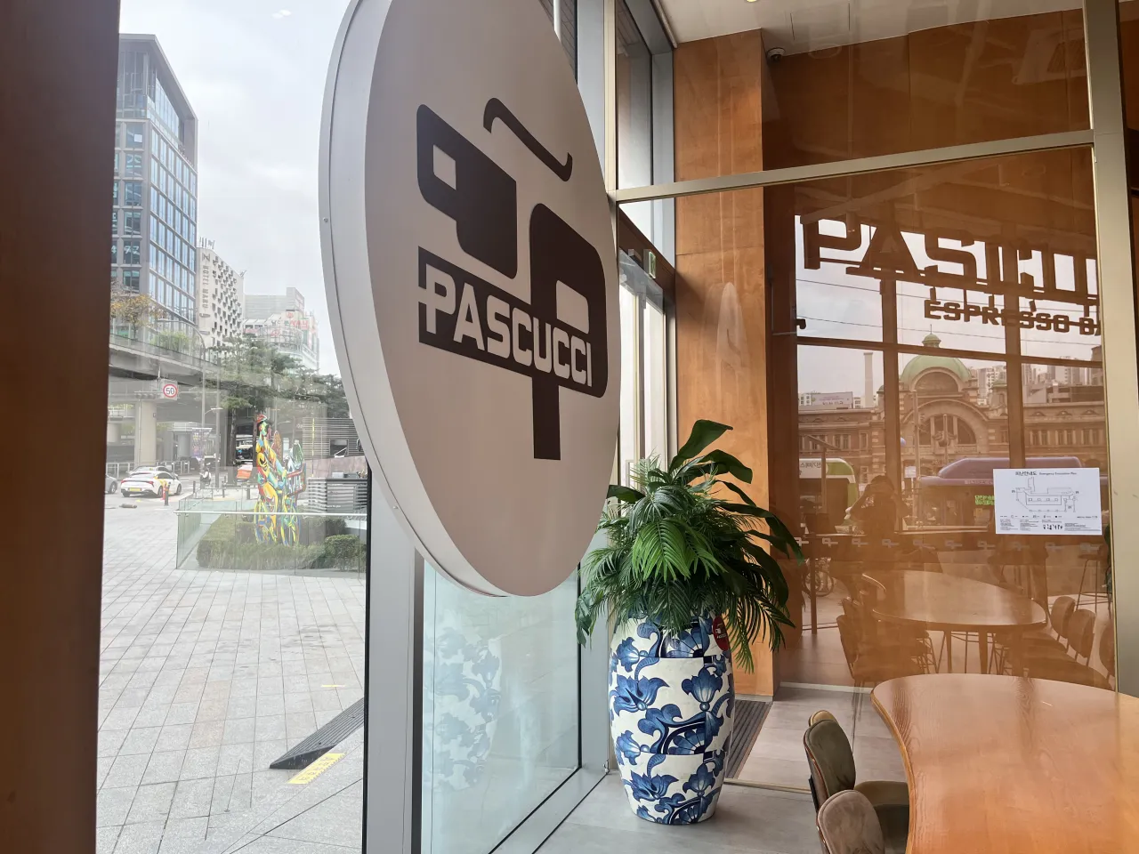 나무-테이블-의자-커다랑-통창-앞에-동그란-파스쿠찌-간판이-있는-카페-실내