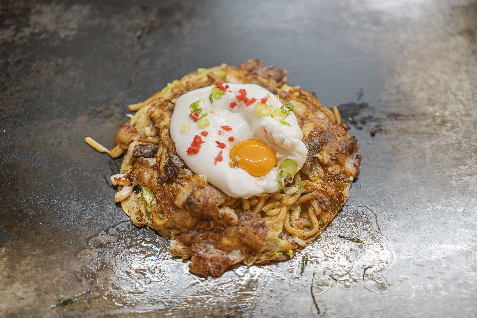 Okonomiyaki no Momo: an egg tops okonomiyaki on an iron plate, with meat and noodles visible.