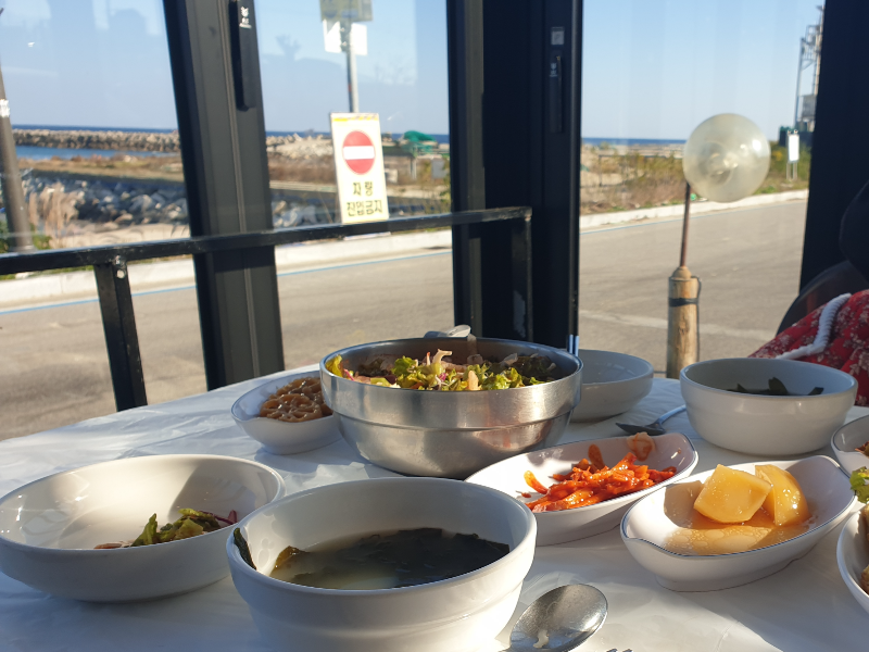 테이블에 주문한 음식이 보이고 창 넘어 바다가 보인다.
