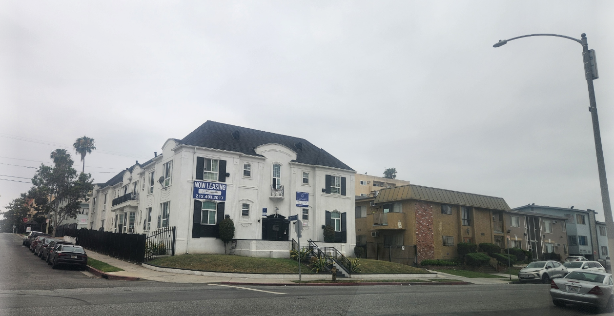 모서리 대지를 차지한 구조로, 'NOW LEASING' 배너가 걸린 클래식 화이트 외관이 특징 아파트 이미지