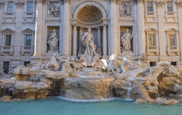 트레비분수 전경이다. 큰 건물 앞에 멋진 사람 조각상들이 서 있고 연못에는 청록색 물이 있다.