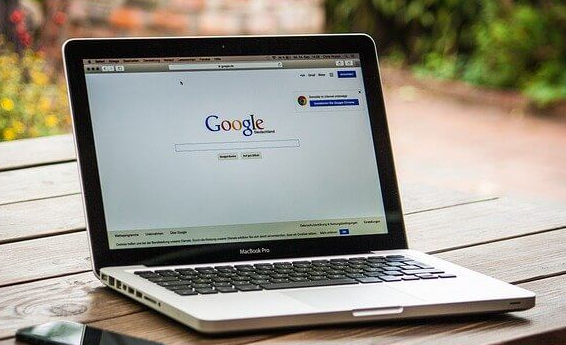 A laptop computer with the Google home page open is placed on a wooden table.